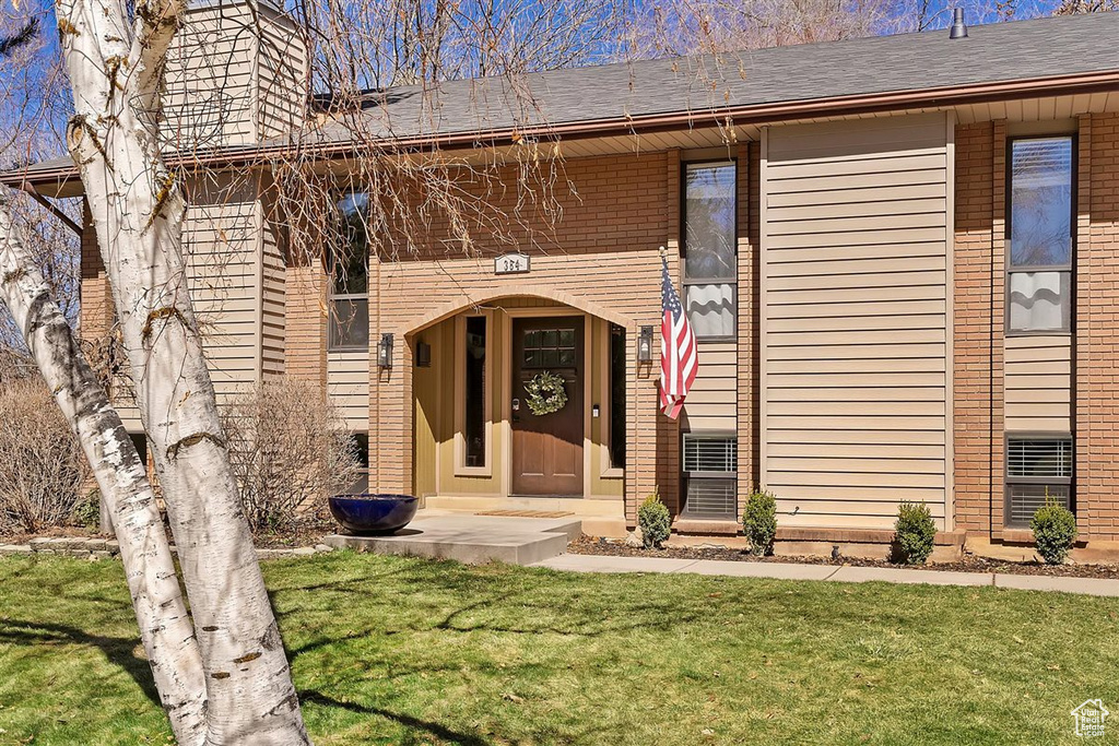 Property entrance with a yard, brick siding, a chimney, and a shingled roof