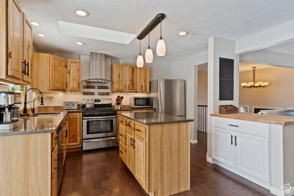 Kitchen featuring wall chimney range hood, stainless steel appliances, a sink, a skylight, and a kitchen island