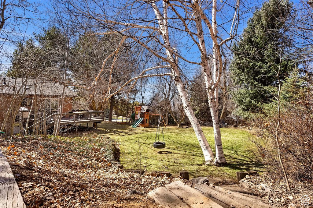 View of grassy yard featuring a playground and a deck