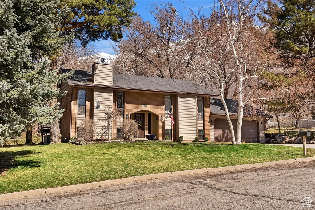 View of front of home with a chimney, a front yard, an attached garage, and concrete driveway