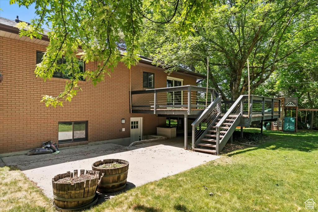 Back of house with a lawn, a patio, brick siding, a wooden deck, and stairway