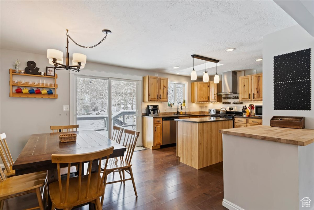 Kitchen with wall chimney range hood, appliances with stainless steel finishes, a kitchen island, dark wood-style flooring, and wood counters