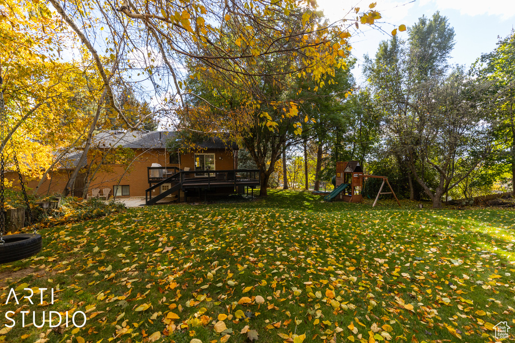 View of green lawn with a playground, a deck, and stairs