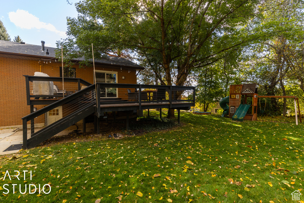 View of grassy yard featuring a playground, a wooden deck, and stairway