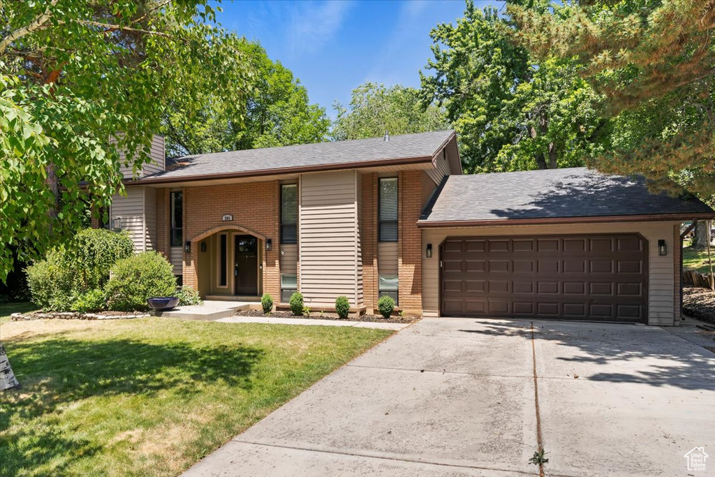 View of front of house featuring a garage, concrete driveway, brick siding, a front yard, and a chimney