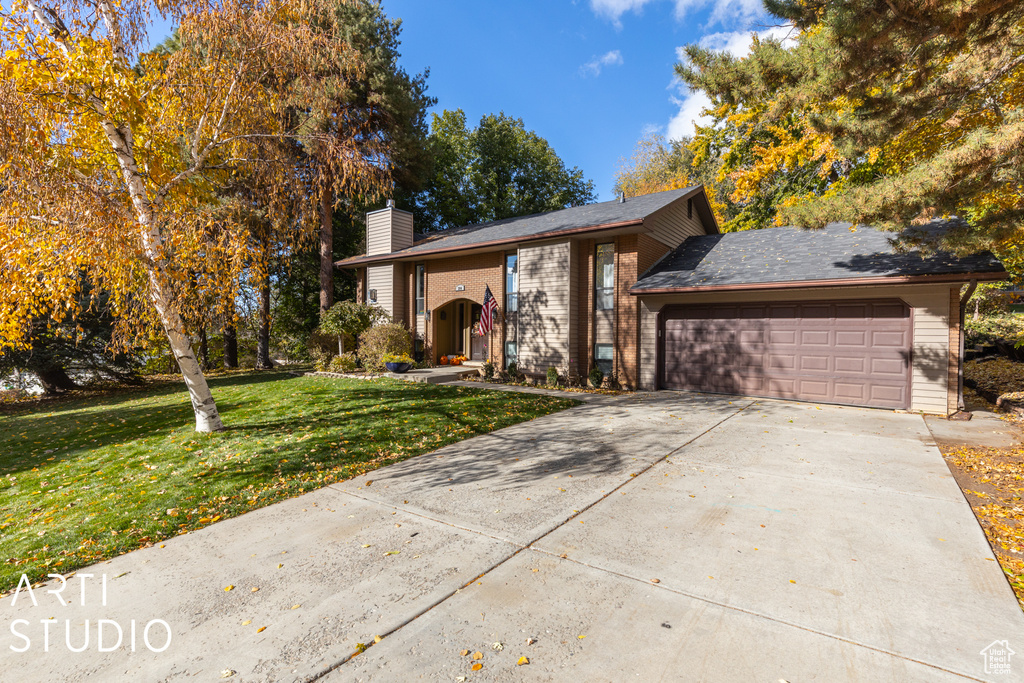 View of front of property with a chimney, an attached garage, brick siding, a front yard, and concrete driveway