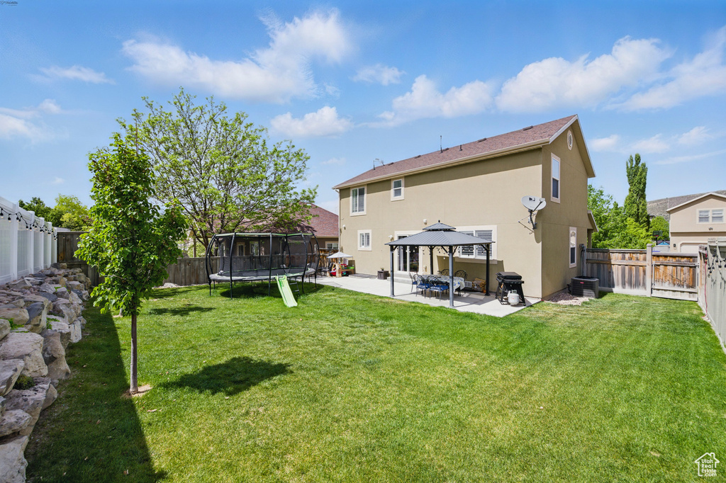 Rear view of property featuring a trampoline, a gazebo, a patio, stucco siding, and central air condition unit