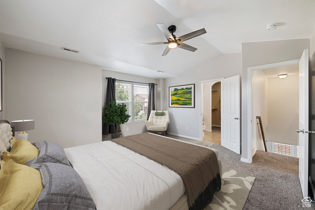 Carpeted bedroom with lofted ceiling, a ceiling fan, and a walk in closet