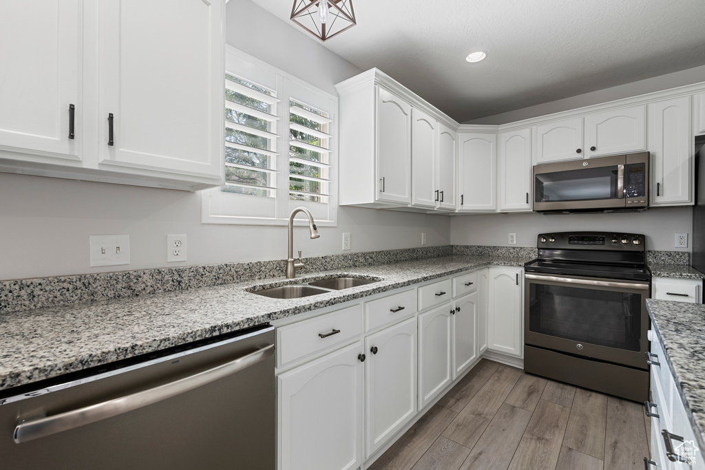 Kitchen featuring appliances with stainless steel finishes, light wood finished floors, white cabinetry, light stone counters, and recessed lighting