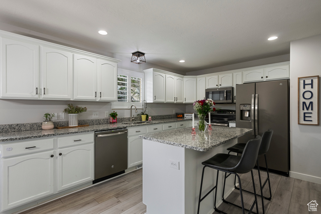 Kitchen with appliances with stainless steel finishes, a sink, white cabinetry, a kitchen breakfast bar, and recessed lighting