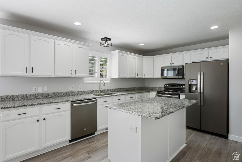 Kitchen with stainless steel appliances, white cabinetry, light wood-type flooring, recessed lighting, and light stone counters