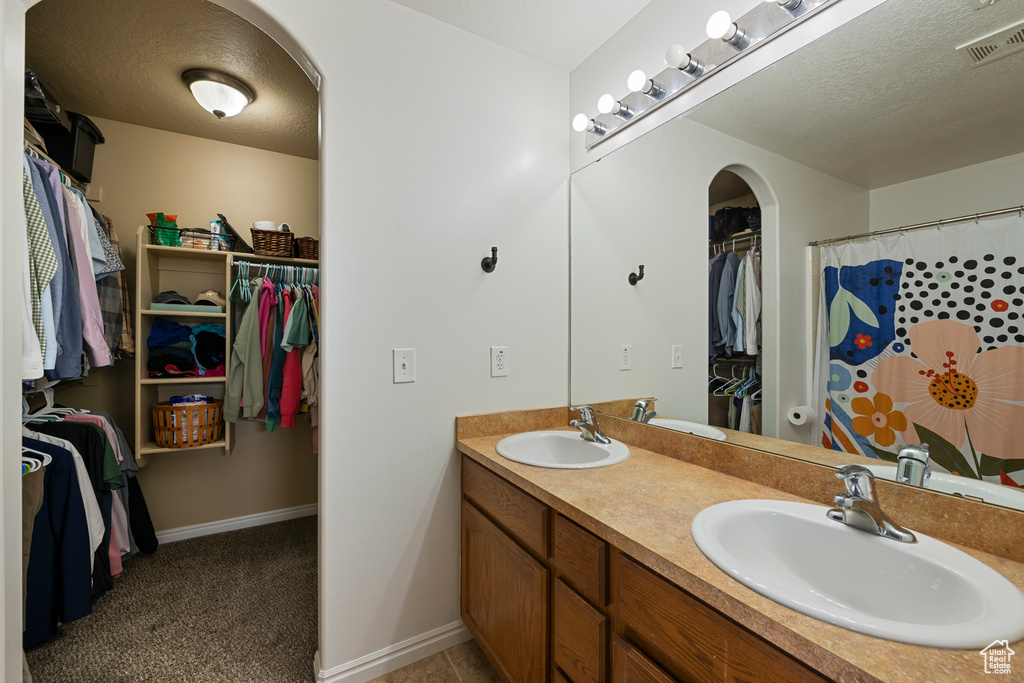 Full bathroom featuring a spacious closet, double vanity, baseboards, and a textured ceiling