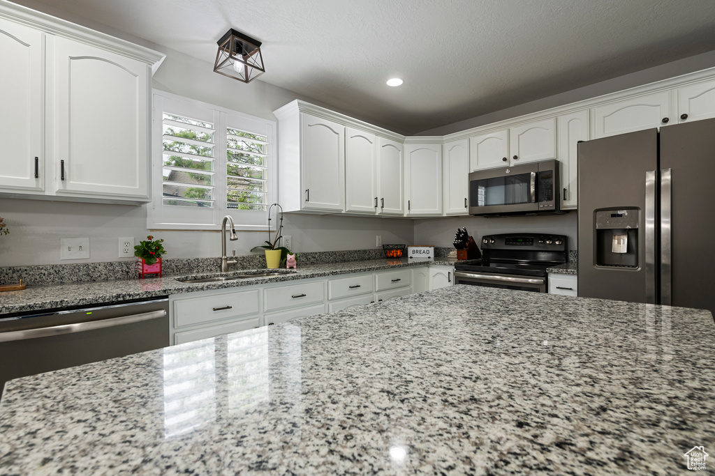 Kitchen featuring stainless steel appliances, a sink, light stone counters, white cabinets, and recessed lighting