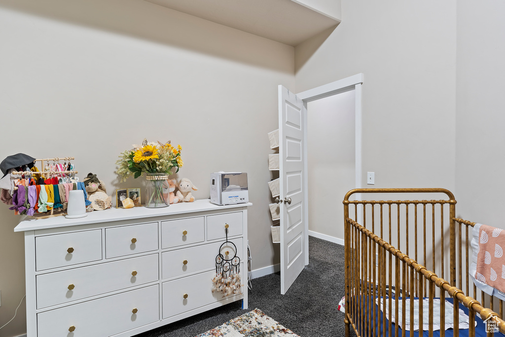 Bedroom with dark carpet, a nursery area, and baseboards