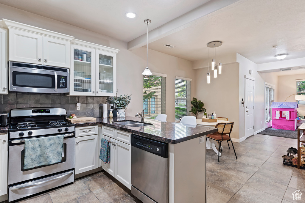 Kitchen with appliances with stainless steel finishes, a sink, decorative backsplash, white cabinetry, and a peninsula