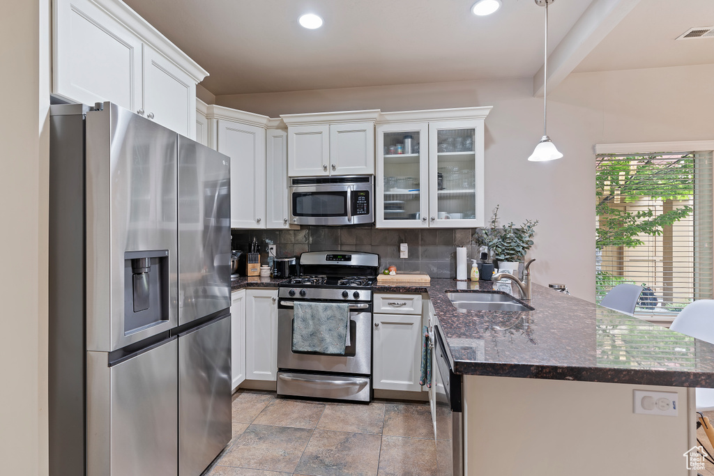 Kitchen with stainless steel appliances, a sink, a peninsula, white cabinets, and tasteful backsplash