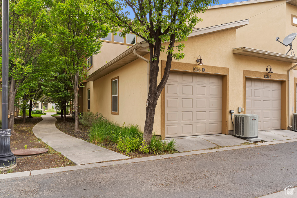 View of side of property with stucco siding, central air condition unit, and a garage
