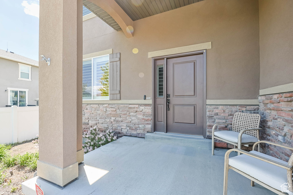 Doorway to property featuring stone siding, stucco siding, fence, and a patio