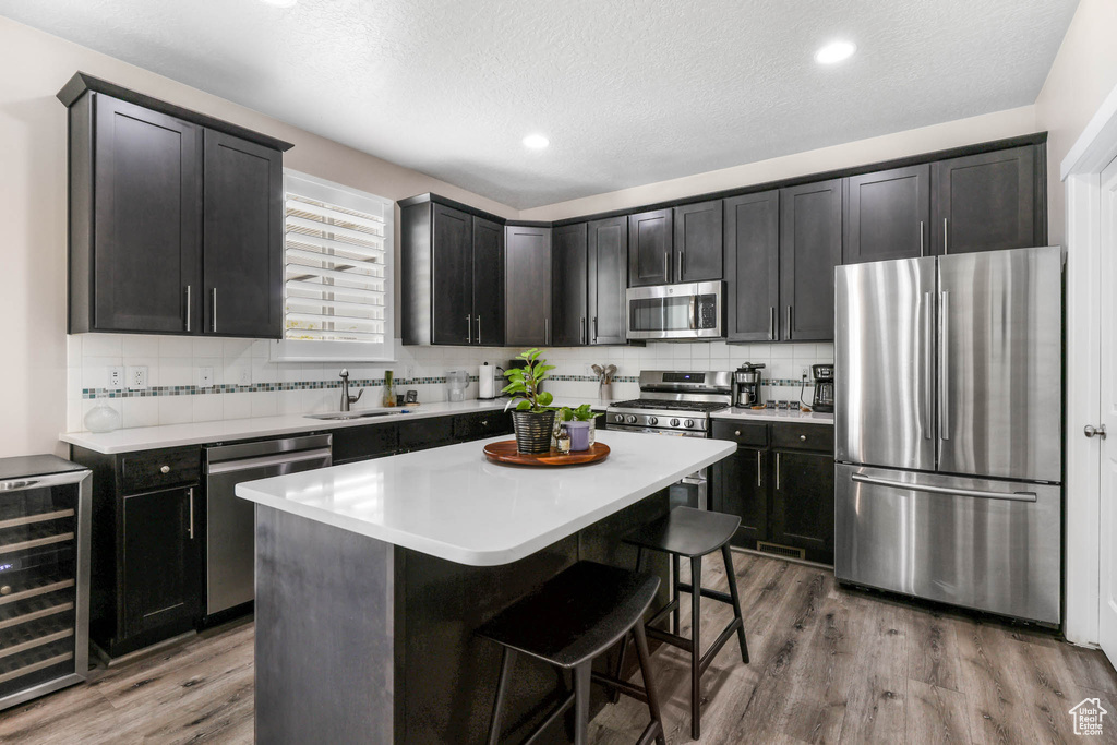 Kitchen featuring appliances with stainless steel finishes, beverage cooler, wood finished floors, a sink, and a textured ceiling