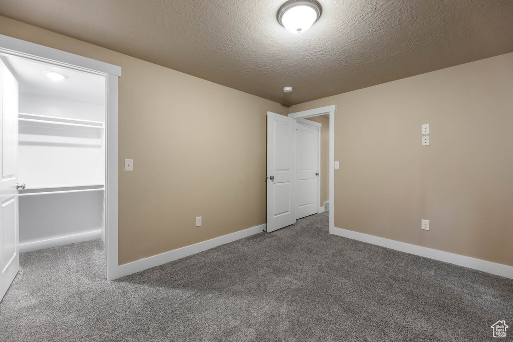 Unfurnished bedroom featuring carpet floors, baseboards, a textured ceiling, and a walk in closet
