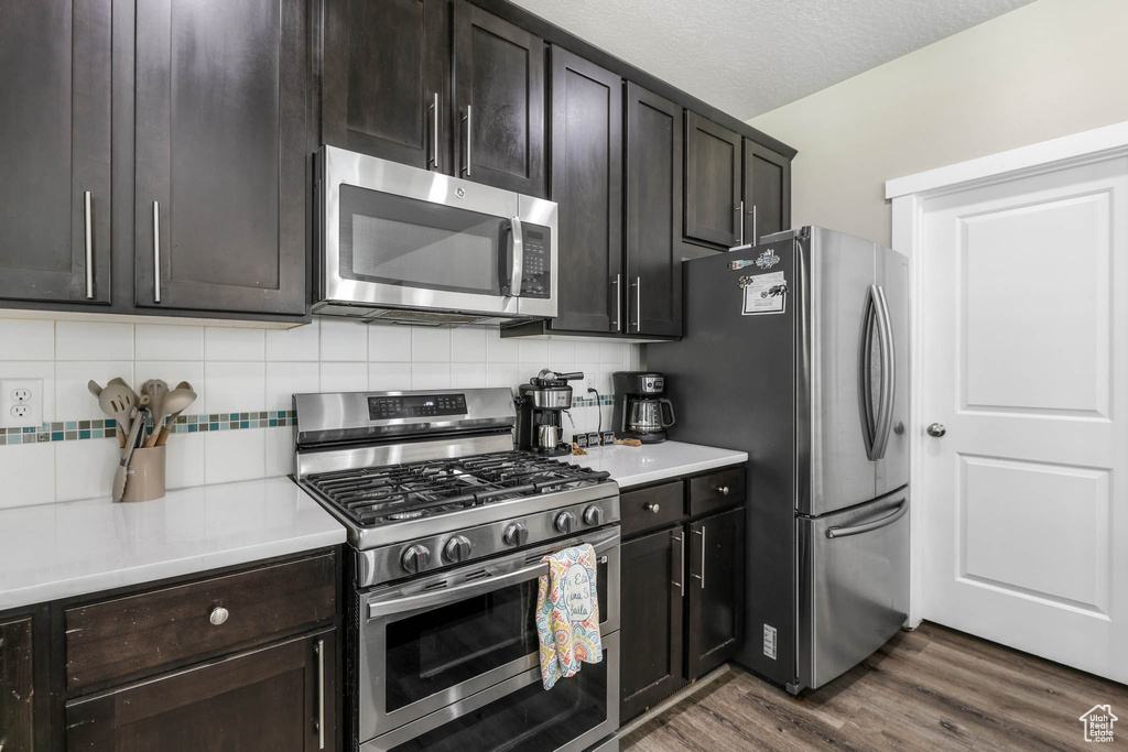Kitchen featuring appliances with stainless steel finishes, tasteful backsplash, dark wood finished floors, and light countertops