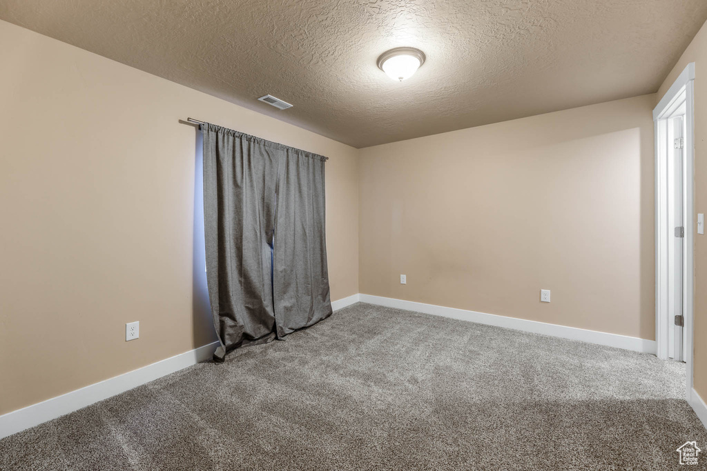 Spare room featuring a textured ceiling, carpet flooring, and baseboards