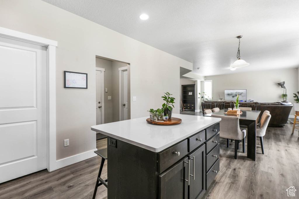 Kitchen featuring dark wood-type flooring, open floor plan, a breakfast bar, decorative light fixtures, and light countertops