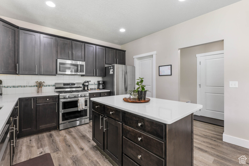 Kitchen with appliances with stainless steel finishes, light wood-style flooring, light countertops, decorative backsplash, and a center island