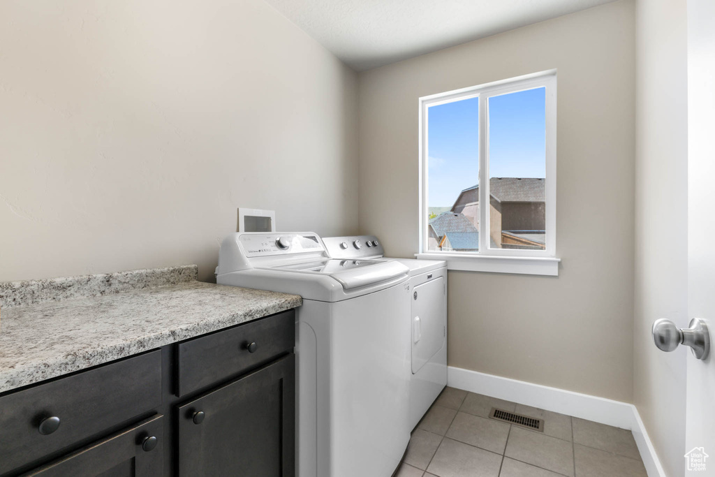Clothes washing area with washer and clothes dryer, baseboards, light tile patterned floors, and cabinet space