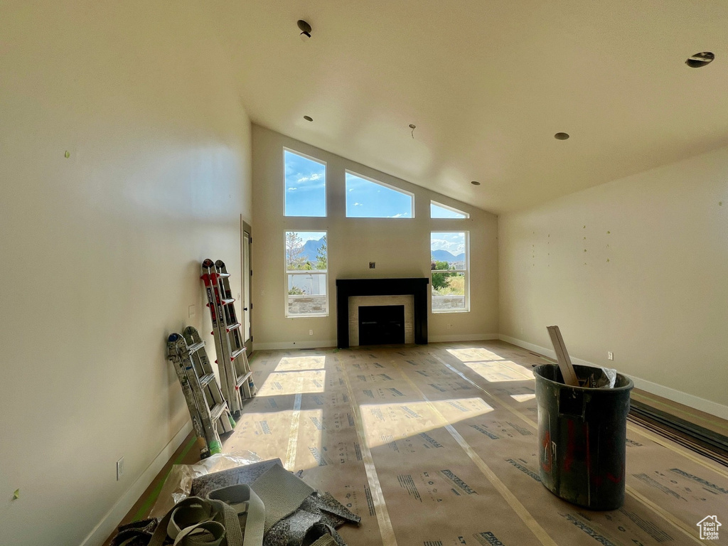 Unfurnished living room featuring a tiled fireplace, baseboards, and high vaulted ceiling
