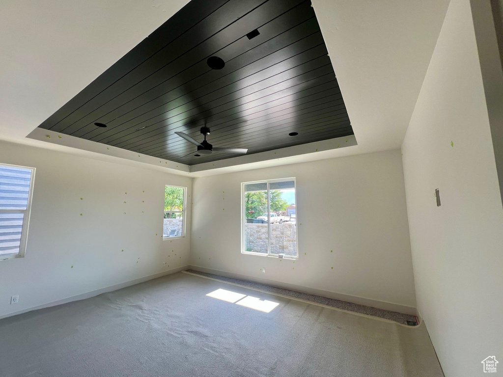 Carpeted empty room with a tray ceiling, wooden ceiling, baseboards, and a ceiling fan