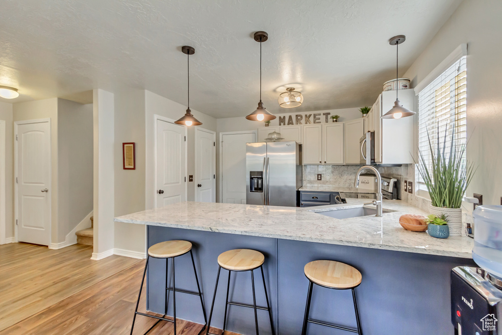 Kitchen with appliances with stainless steel finishes, a peninsula, light wood-style flooring, light stone countertops, and a kitchen bar