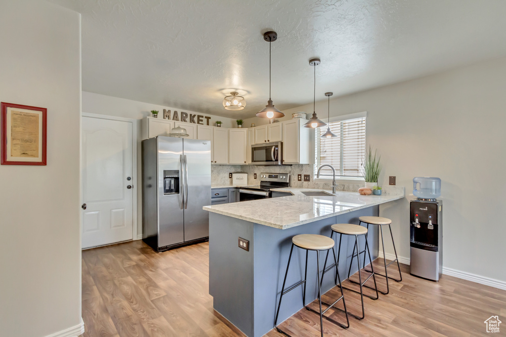 Kitchen featuring appliances with stainless steel finishes, a peninsula, a breakfast bar area, light wood-style floors, and a textured ceiling