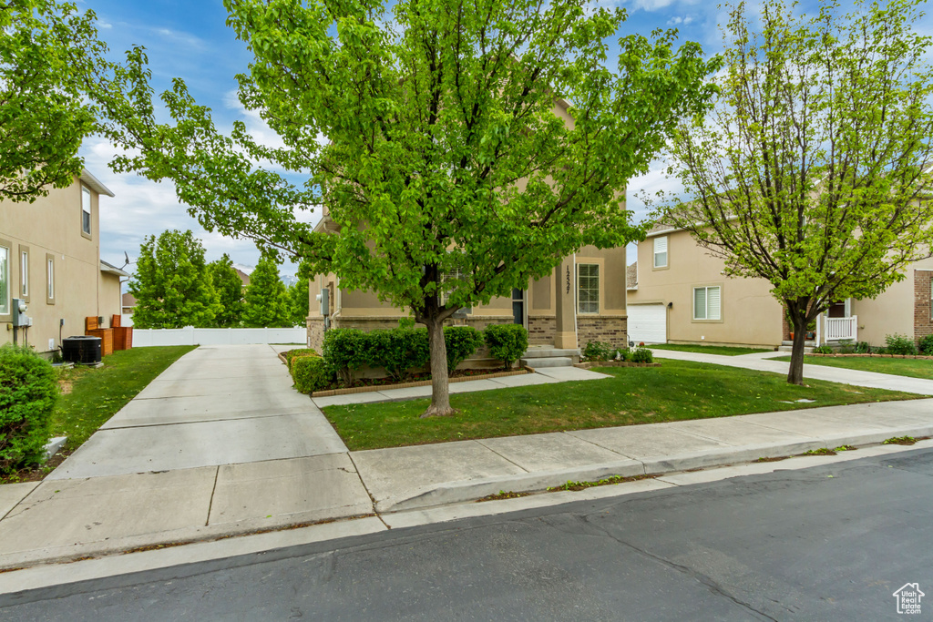 View of property hidden behind natural elements featuring a front lawn, central air condition unit, and stucco siding