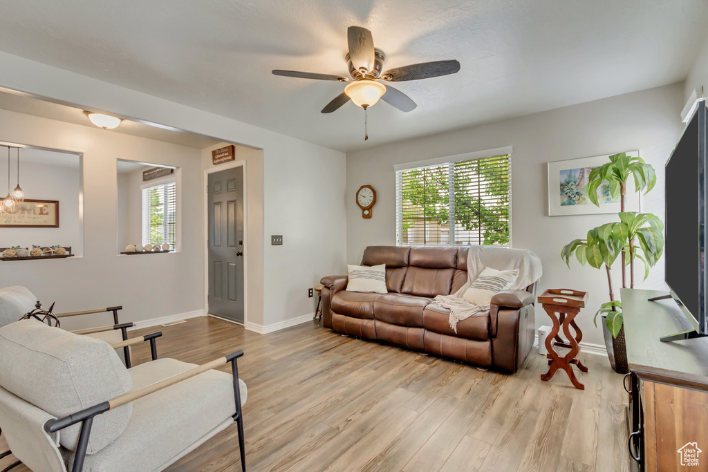 Living area featuring plenty of natural light, light wood finished floors, baseboards, and a ceiling fan