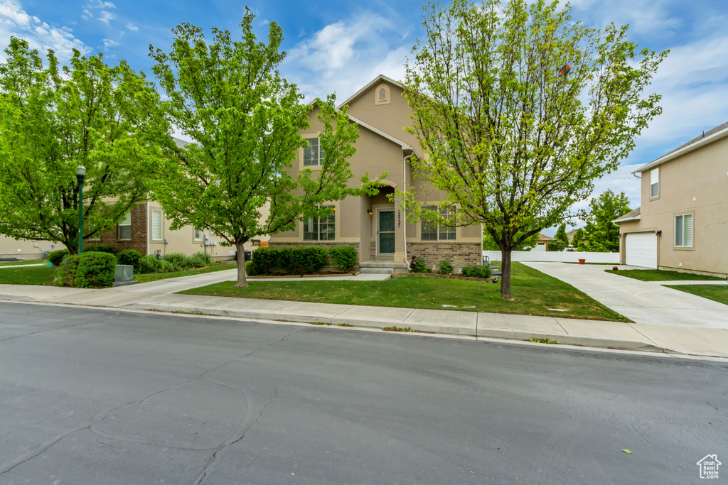 View of property hidden behind natural elements featuring stucco siding, brick siding, a front yard, driveway, and a garage