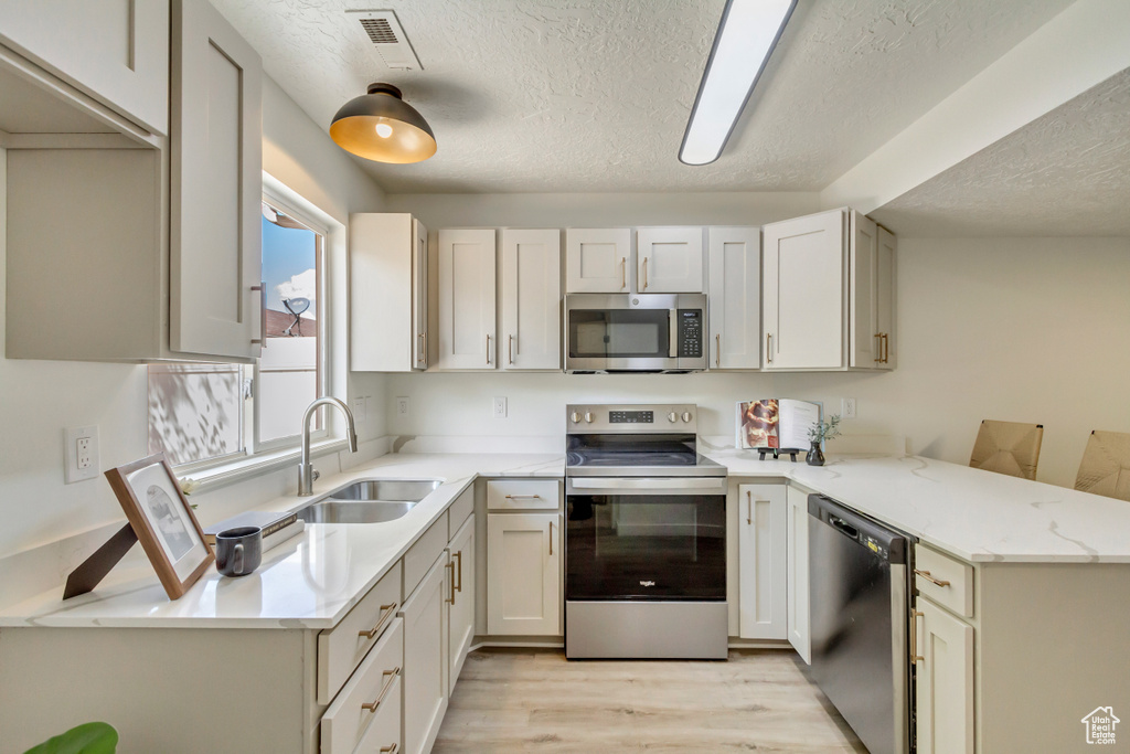 Kitchen featuring stainless steel appliances, a textured ceiling, a sink, a peninsula, and light wood-style floors