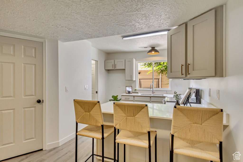 Kitchen with a textured ceiling, a sink, gray cabinets, a peninsula, and a breakfast bar