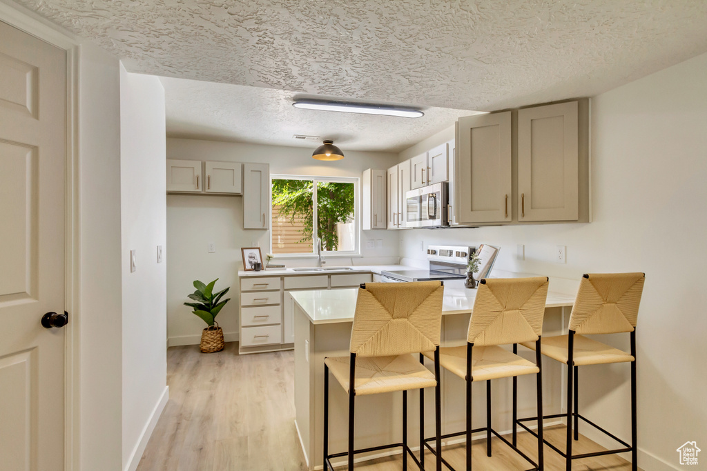 Kitchen with stainless steel microwave, white range with electric cooktop, a sink, a peninsula, and a breakfast bar