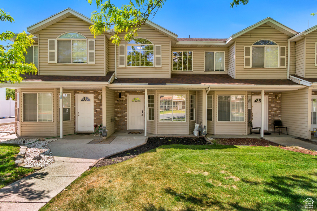 Townhome / multi-family property featuring a front yard, roof with shingles, brick siding, and a porch