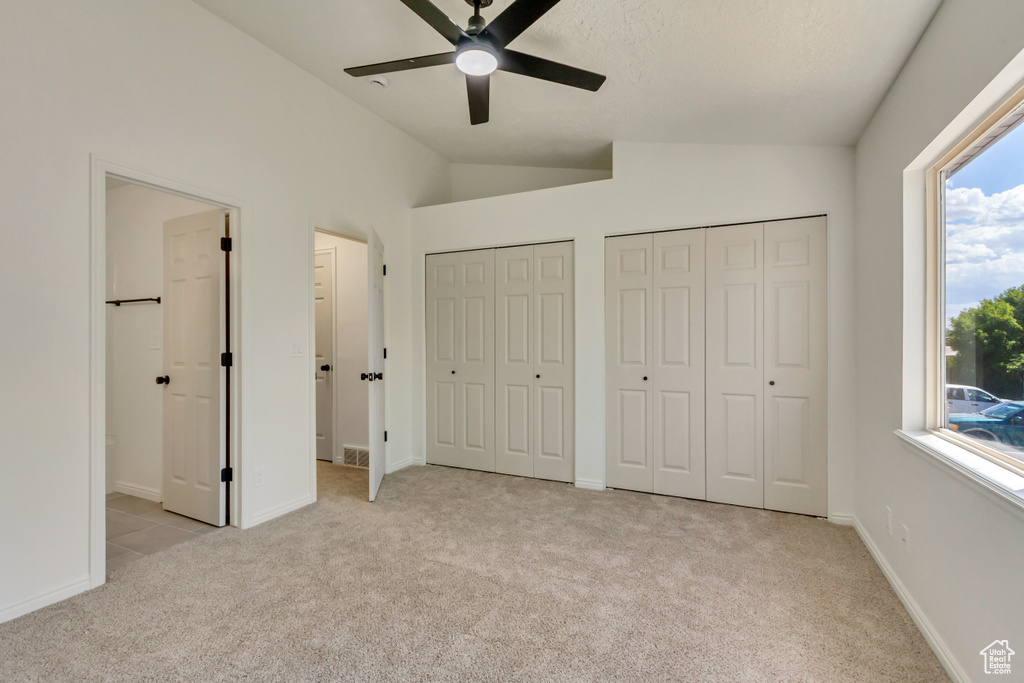 Unfurnished bedroom with light colored carpet, vaulted ceiling, two closets, connected bathroom, and ceiling fan
