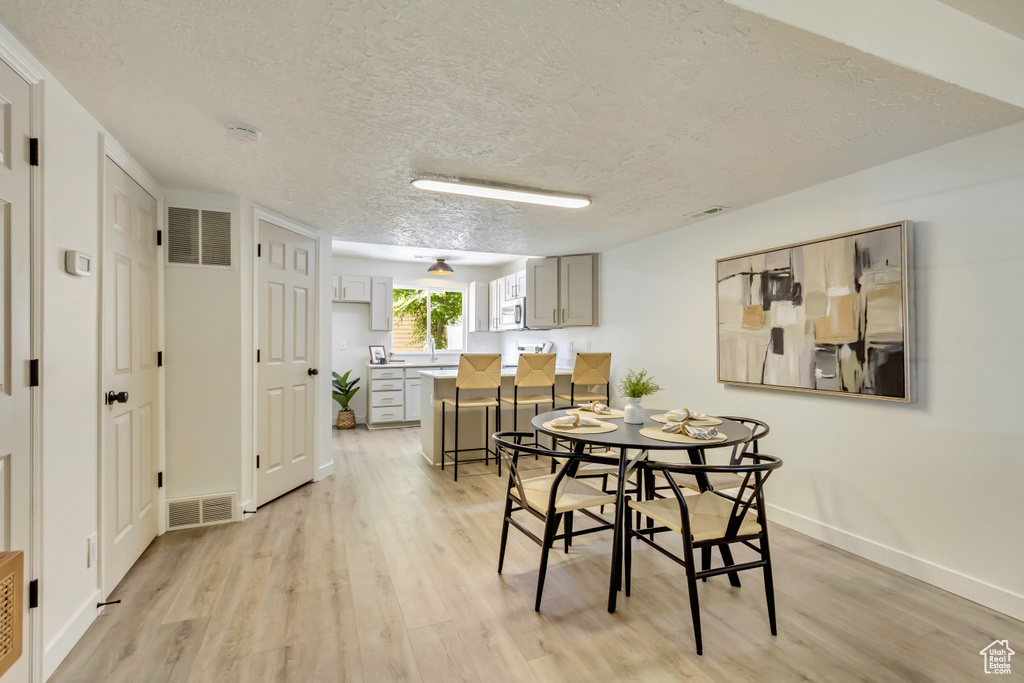 Dining room featuring light wood-style floors, a textured ceiling, and baseboards