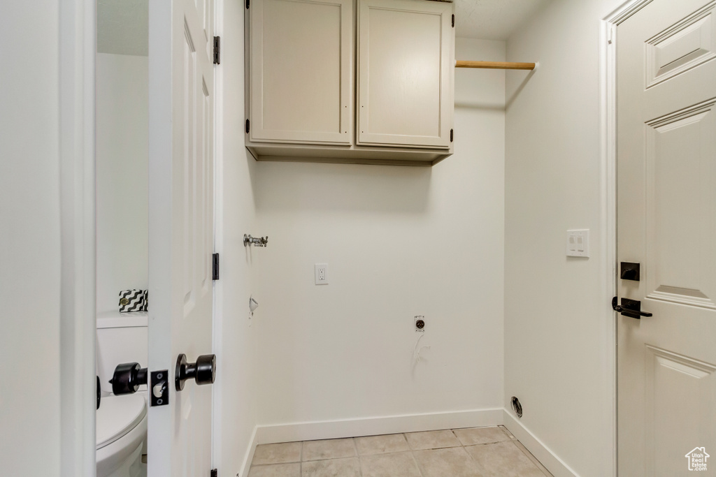 Laundry area featuring electric dryer hookup, baseboards, cabinet space, and light tile patterned floors