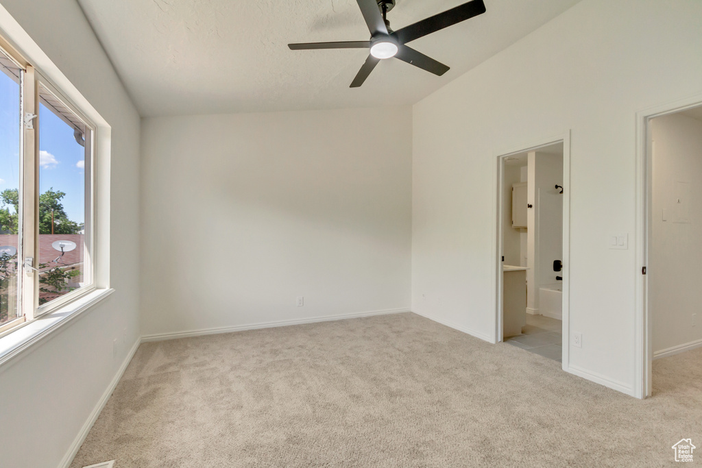 Empty room with light colored carpet, a ceiling fan, vaulted ceiling, baseboards, and a textured ceiling