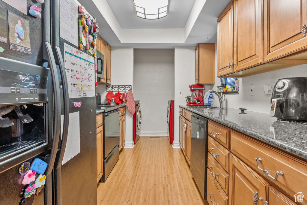Kitchen featuring black appliances, light wood-type flooring, washer / clothes dryer, a sink, and brown cabinets
