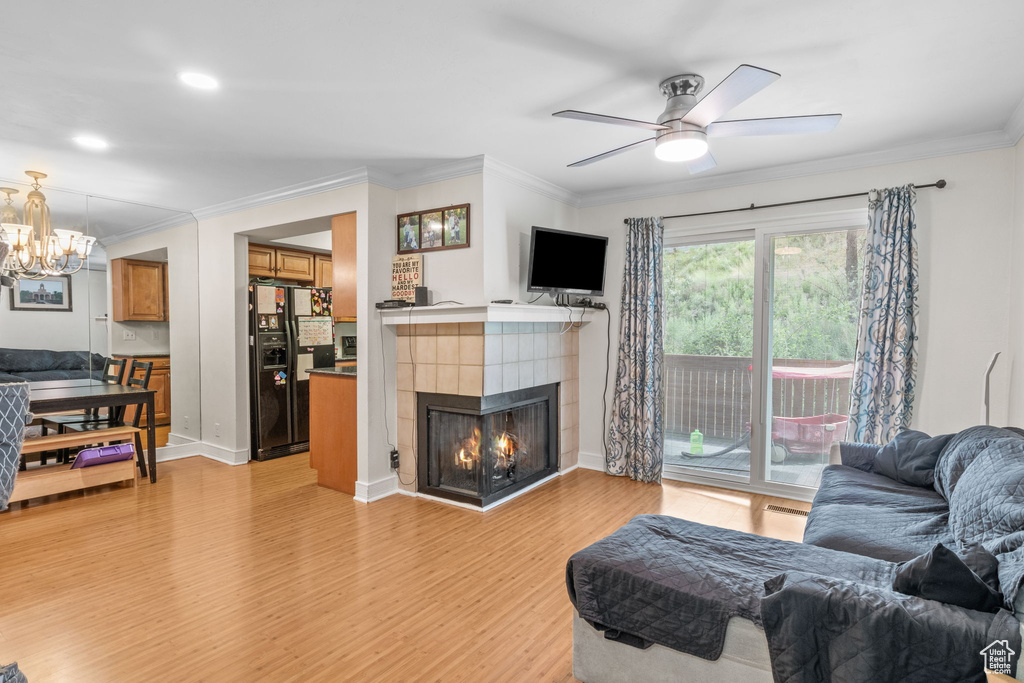 Living area featuring light wood-type flooring, ornamental molding, a tile fireplace, ceiling fan, and a chandelier