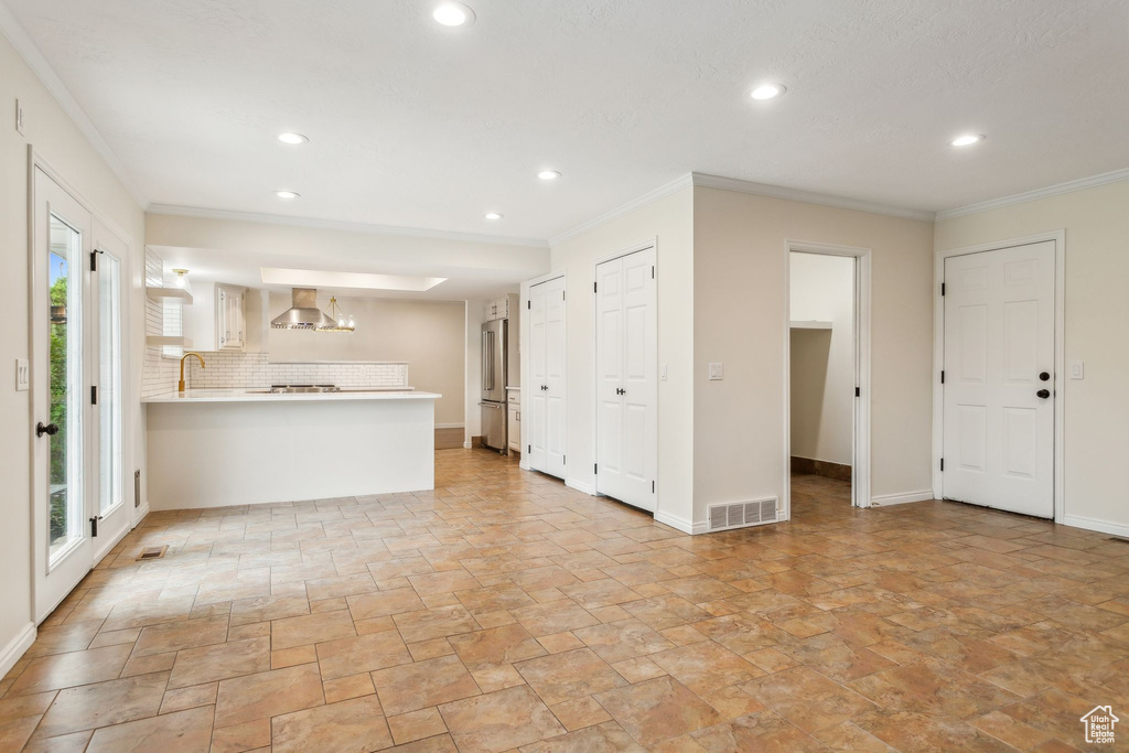Unfurnished living room featuring stone tile floors, recessed lighting, a sink, ornamental molding, and baseboards