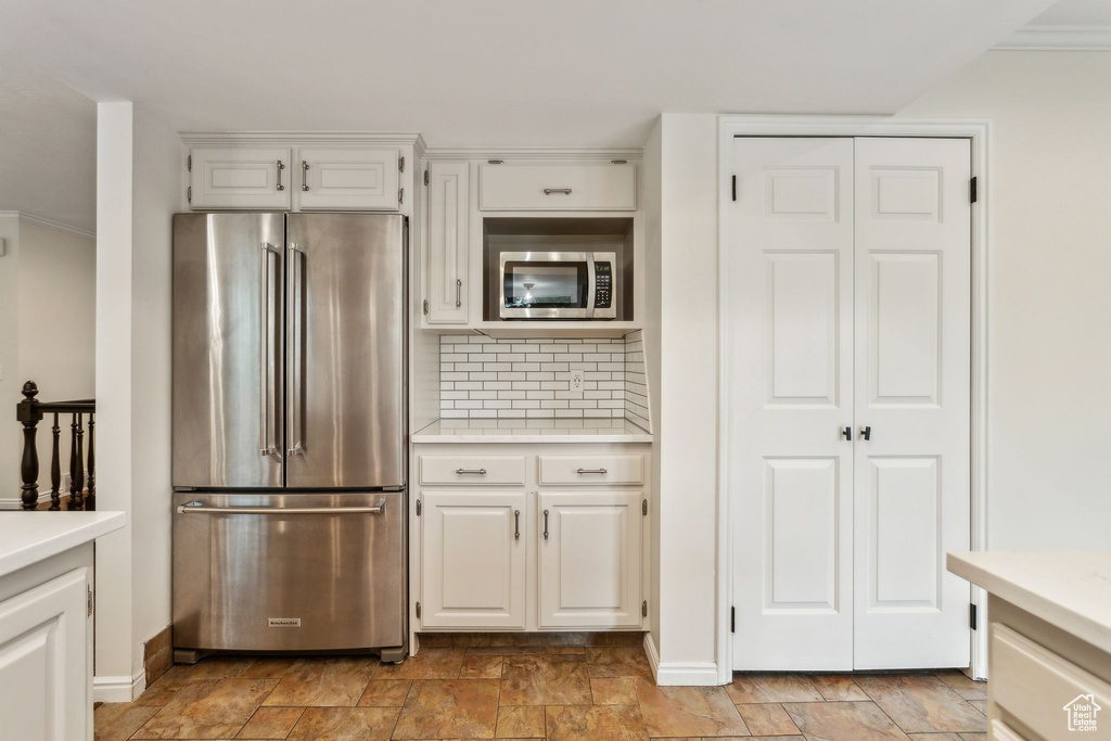 Kitchen featuring appliances with stainless steel finishes, light countertops, stone finish flooring, white cabinets, and ornamental molding
