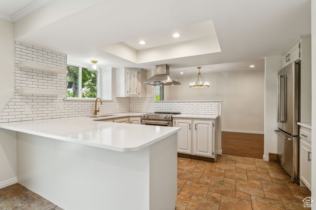 Kitchen featuring a peninsula, wall chimney range hood, a sink, premium appliances, and light stone finish flooring