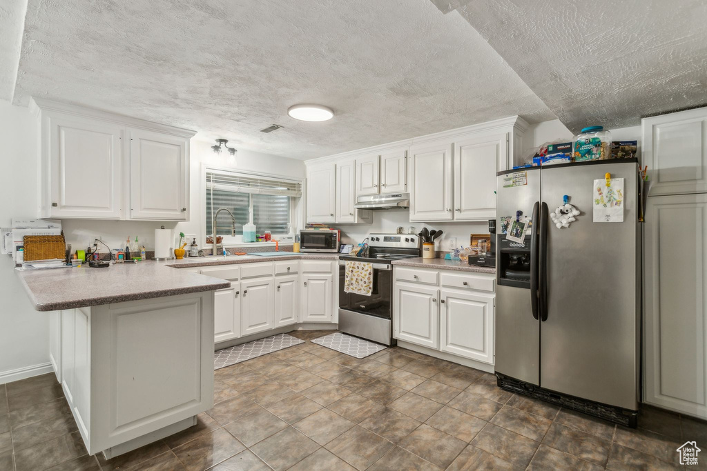 Kitchen featuring appliances with stainless steel finishes, under cabinet range hood, a peninsula, white cabinetry, and a textured ceiling